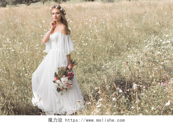 一个美丽的女孩穿着白色的裙子在拍照美丽的沉思年轻新娘在婚礼礼服和花卉花圈举行鲜花, 而站在户外